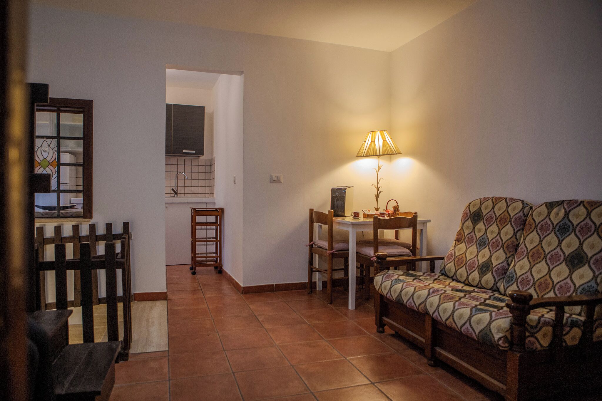 Uma sala de estar aconchegante com um sofá, uma mesa de jantar e cadeiras. Há uma luminária sobre a mesa e um banco de madeira no canto.