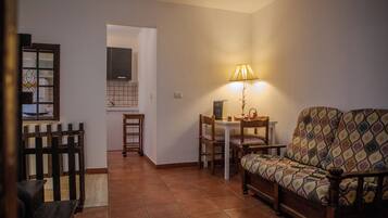 Uma sala de estar aconchegante com um sofá, uma mesa de jantar e cadeiras. Há uma luminária sobre a mesa e um banco de madeira no canto.