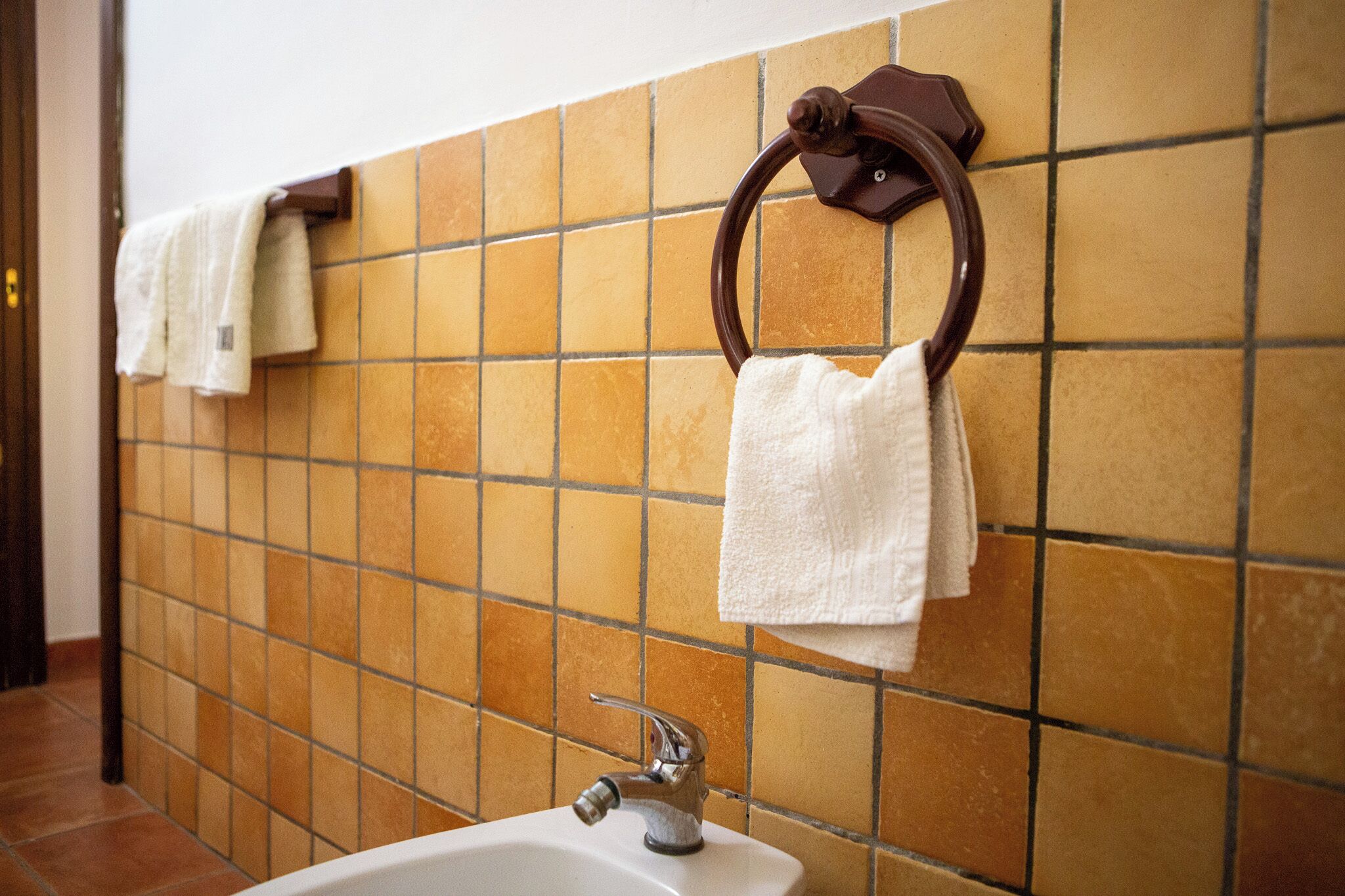 A bathroom with a tiled wall, a sink, and two towel rings with white towels.