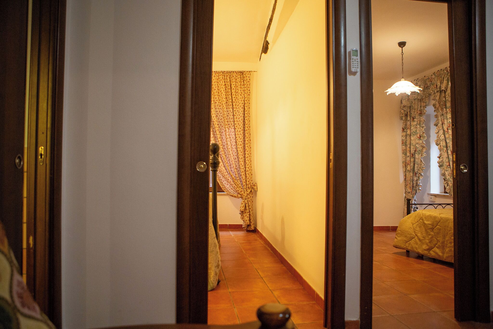 A hallway leading to a bedroom with a bed, a door, and a curtain.