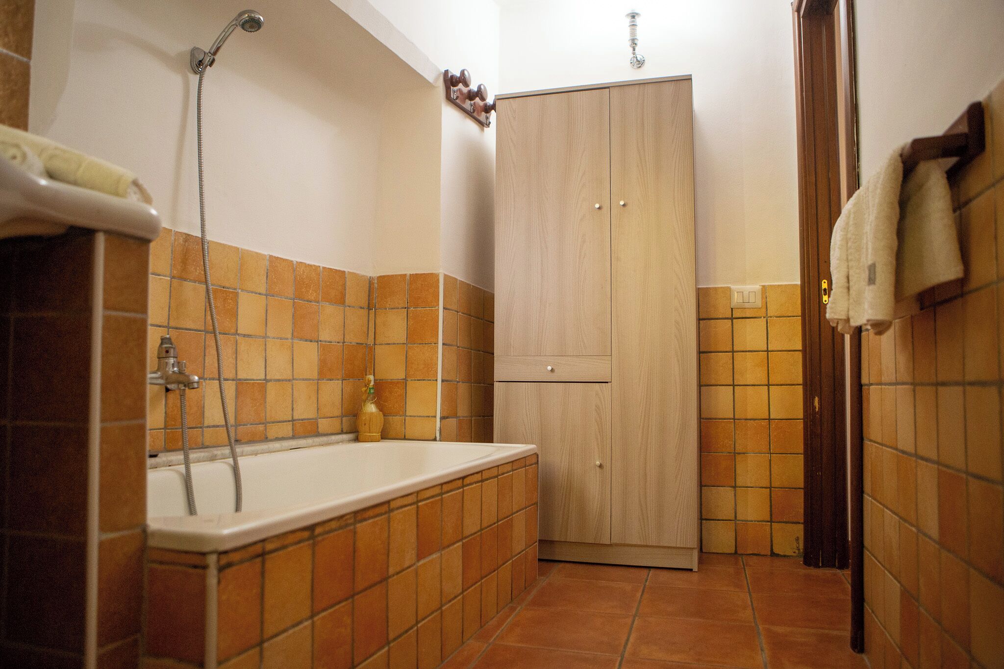 Een badkamer met een bad, een houten kledingkast en betegelde muren.