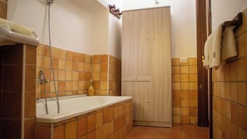 Een badkamer met een bad, een houten kledingkast en betegelde muren.