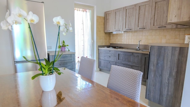 A modern kitchen with wooden cabinets, a stainless steel refrigerator, and a dining table with a potted orchid. - Casa Carmen (Capaccio-Paestum)