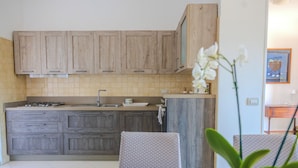 A kitchen with wooden cabinets, a countertop, and a dining area with a table and chairs. - Casa Carmen (Capaccio-Paestum)