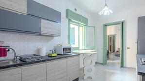 Una cocina moderna con armarios grises, una encimera blanca y un microondas. Hay una ventana con detalles verdes y una lámpara colgante.