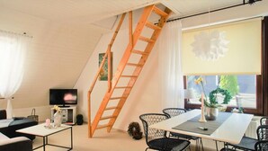 Una habitación estilo loft con una escalera de madera, una mesa de comedor, sillas, un televisor y una ventana con vistas a la vegetación.