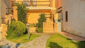 A two-story building with a stone pathway leading to the entrance, surrounded by greenery and a clear blue sky. - Casa Puni (Olbia)