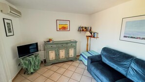 A living room with a flat-screen TV, a green cabinet, a blue sofa, a floor lamp, and a bookshelf. - Casa Puni (Olbia)