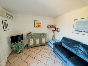 A living room with a flat-screen TV, a green cabinet, a blue sofa, a floor lamp, and a bookshelf. - Casa Puni (Olbia)