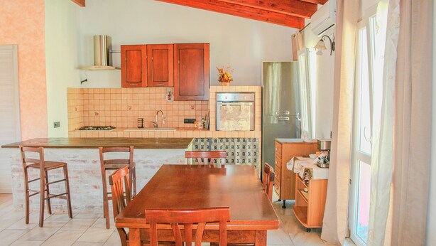 Una cocina con armarios de madera, salpicadero de azulejos, un refrigerador y un comedor con mesa y sillas.