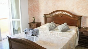 Una cama bien hecha con cabecera de madera, una mesita de noche con lámpara y una cesta de toallas en la mesita.