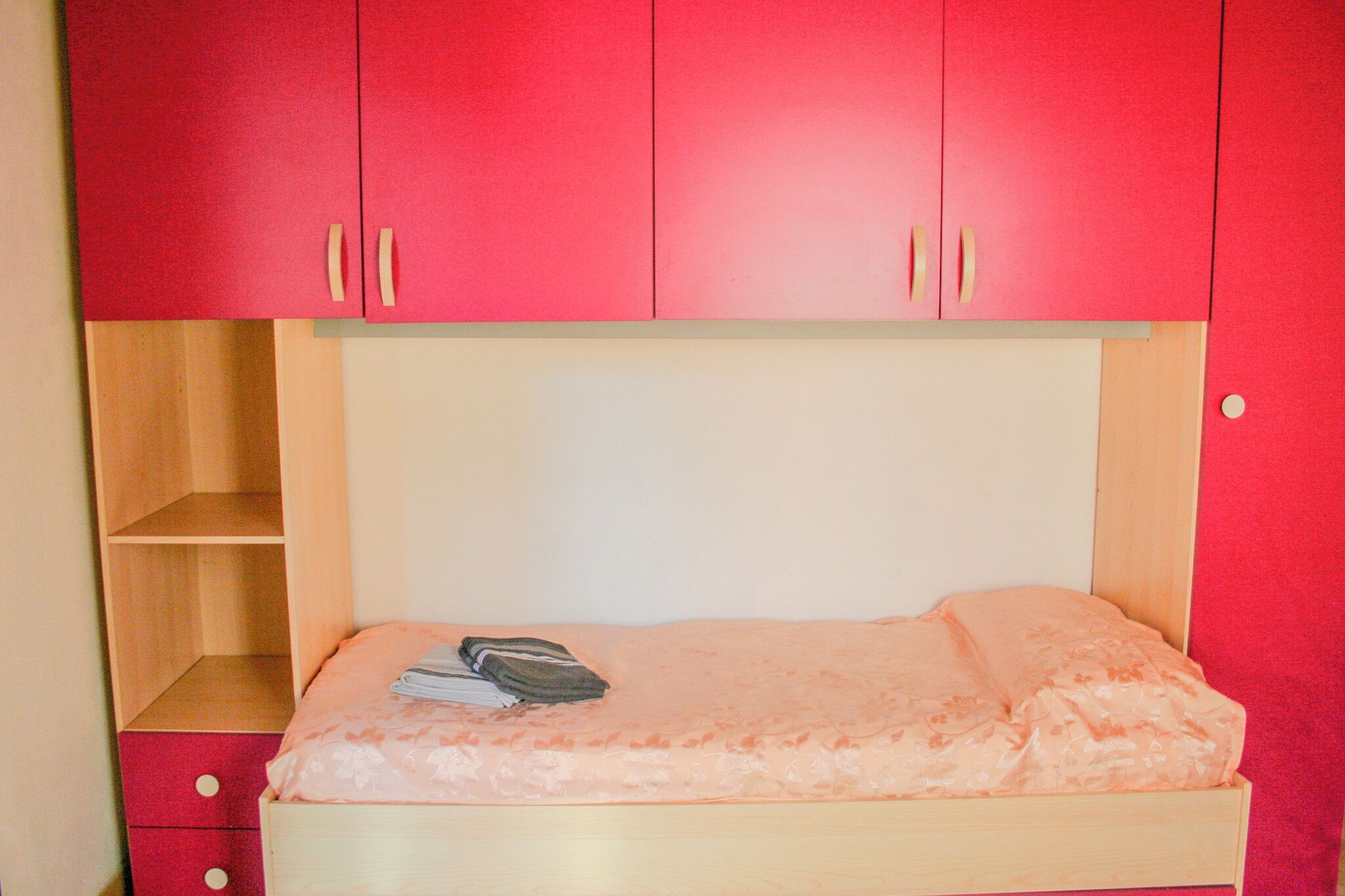 A single bed with a wooden headboard and a red wardrobe above it.
