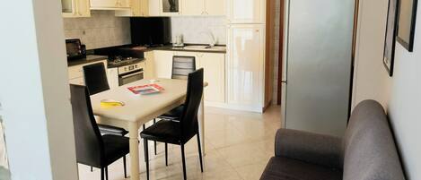 A compact kitchen with a dining area, including a table with chairs, a sofa, and a refrigerator.