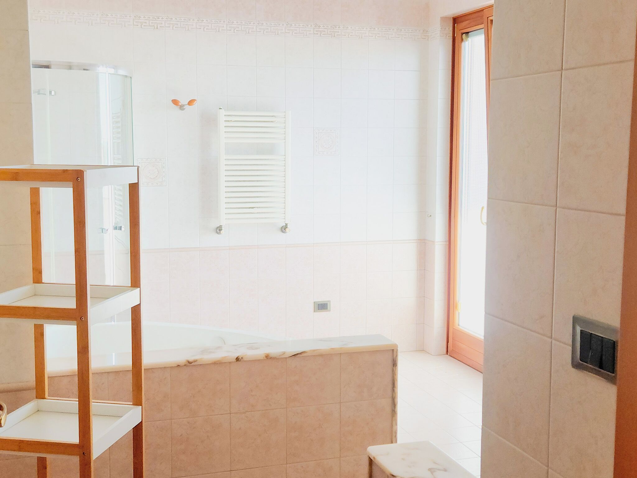 Un bagno con una vasca, uno scaffale in legno e una finestra.