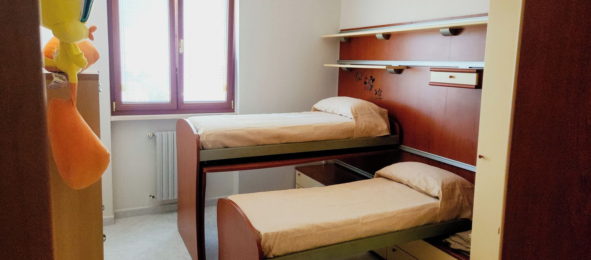 A dormitory room with two bunk beds, a window, and a radiator.