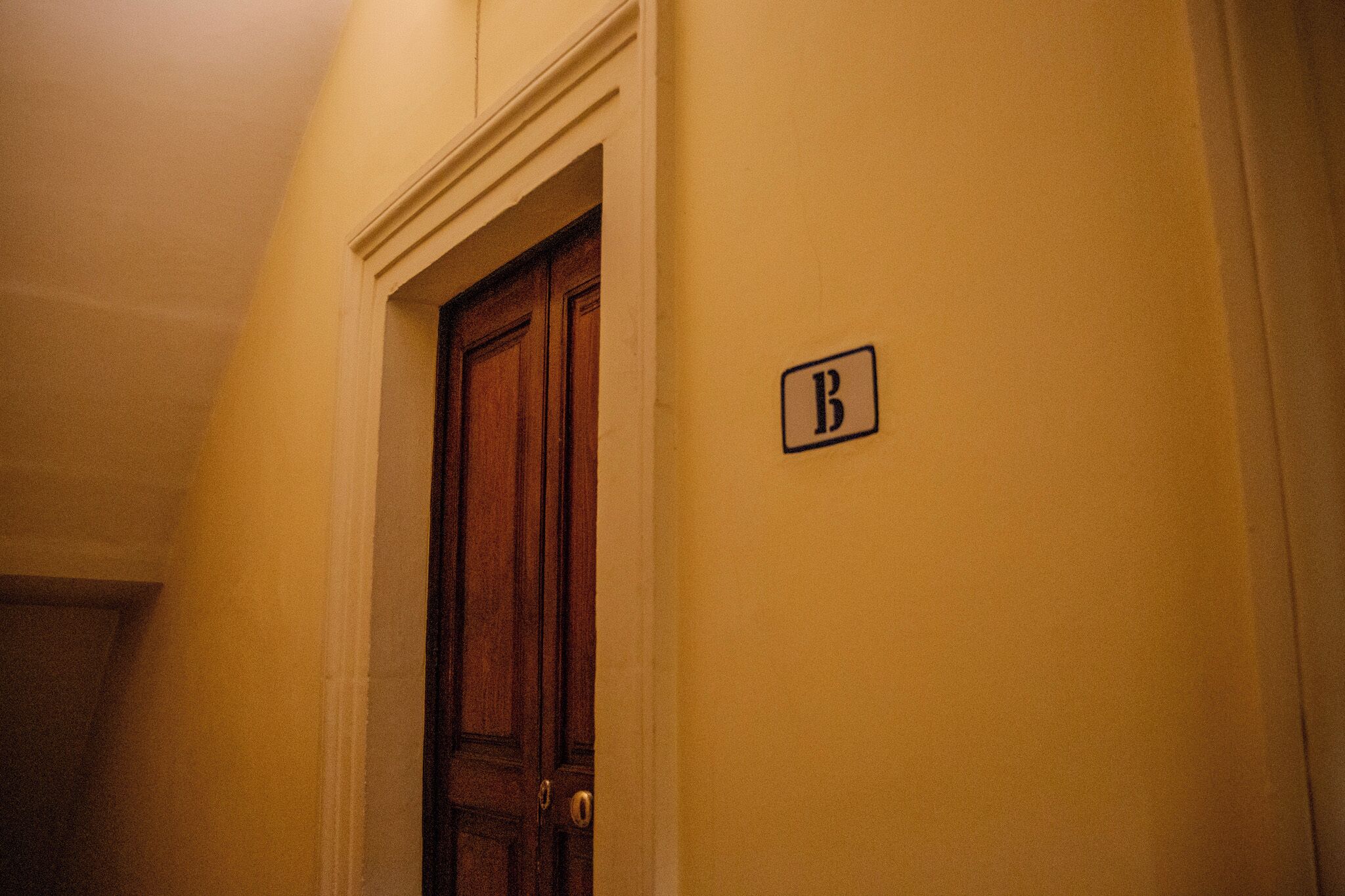 A hallway with a wooden door and a sign with the letter 'B' on the wall.