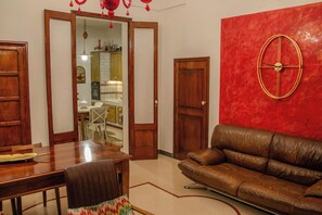 A living room with a brown leather sofa, a wooden dining table, and chairs. There is a red accent wall with a clock. - Agata 1913 (Galatina)
