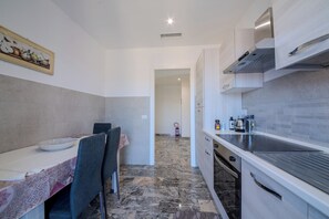 A compact kitchen with a dining area, featuring a marble floor, white cabinetry, and a painting on the wall. - Magnolia House - Appartamento 1 (Fonte Nuova)