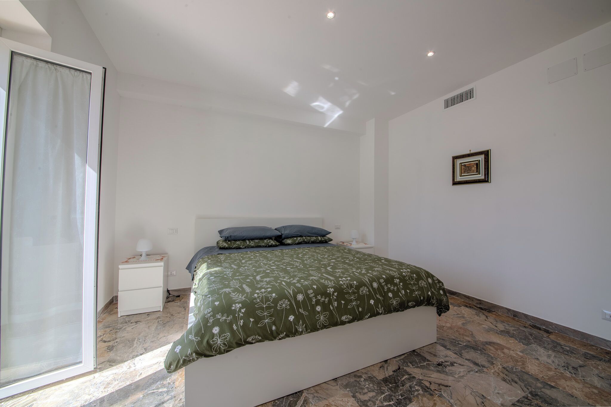 A bedroom with a bed, nightstands, a window with curtains, and a framed picture on the wall.