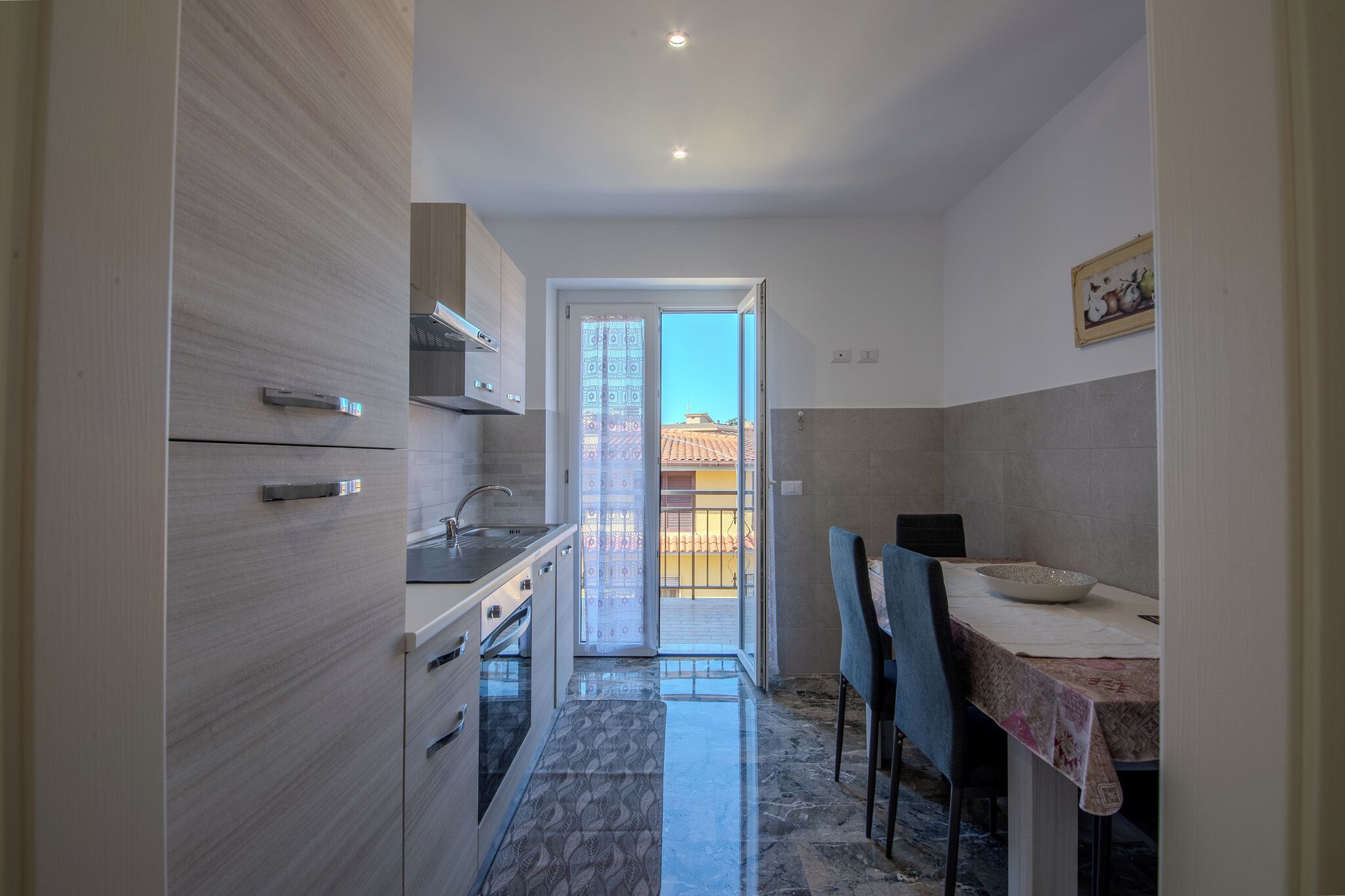 Una cucina compatta con zona pranzo, una porta scorrevole in vetro che dà su un balcone e un piccolo tavolo con una ciotola.