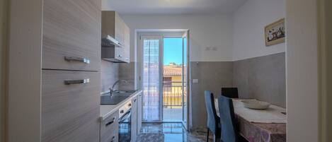 Una cucina compatta con zona pranzo, una porta scorrevole in vetro che dà su un balcone e un piccolo tavolo con una ciotola.