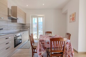 A modern kitchen with wooden cabinets, a built-in oven, and a dining area with a table set for four. - Magnolia House - Appartamento 2 (Fonte Nuova)