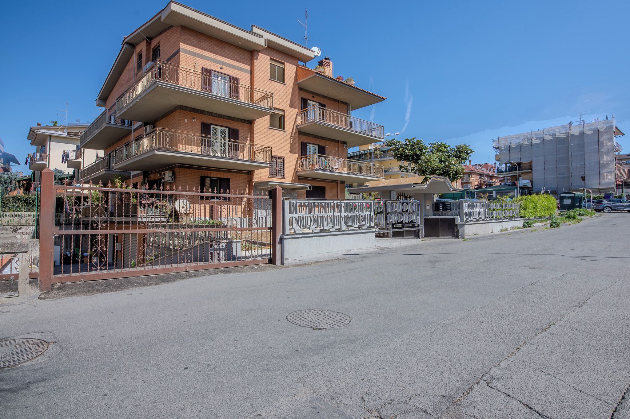 Un edificio residencial de varios pisos con balcones, una entrada con portón y un cielo despejado.