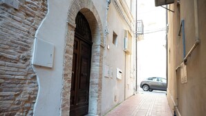 Un callejón estrecho con un edificio de ladrillo a la izquierda y uno de color beige a la derecha. Un coche está estacionado al final del callejón.