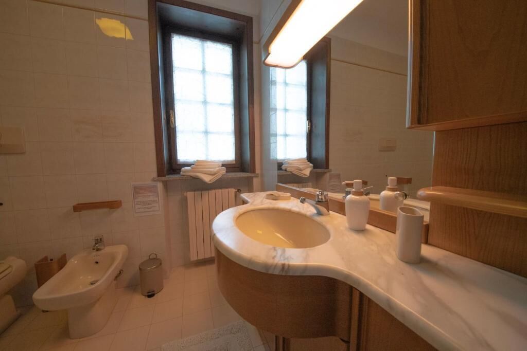 Un baño moderno con un lavamanos curvo, un bidé, una ventana con toallas y un espejo.