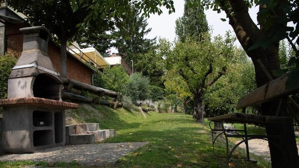 Un espacio al aire libre con un horno de piedra, un banco de concreto y una mesa de metal.