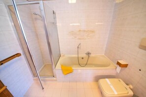 A bathroom with a glass shower enclosure, a bathtub with a yellow towel, and a toilet. - La Collina Di Pavarolo (Pavarolo)