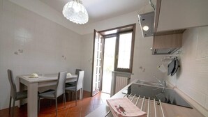 Cocina compacta con mesa, sillas, lámpara colgante y ventana que proporciona luz natural.