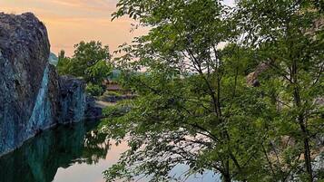 A serene landscape with a calm body of water reflecting the sky, surrounded by lush greenery and rocky formations.