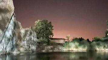 A nighttime view of a calm body of water reflecting a rocky landscape with a tree and a building.