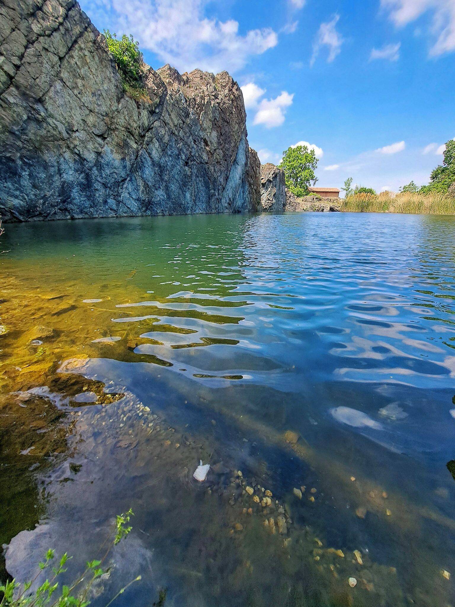 A clear lake with rocky cliffs and a small building in the background.