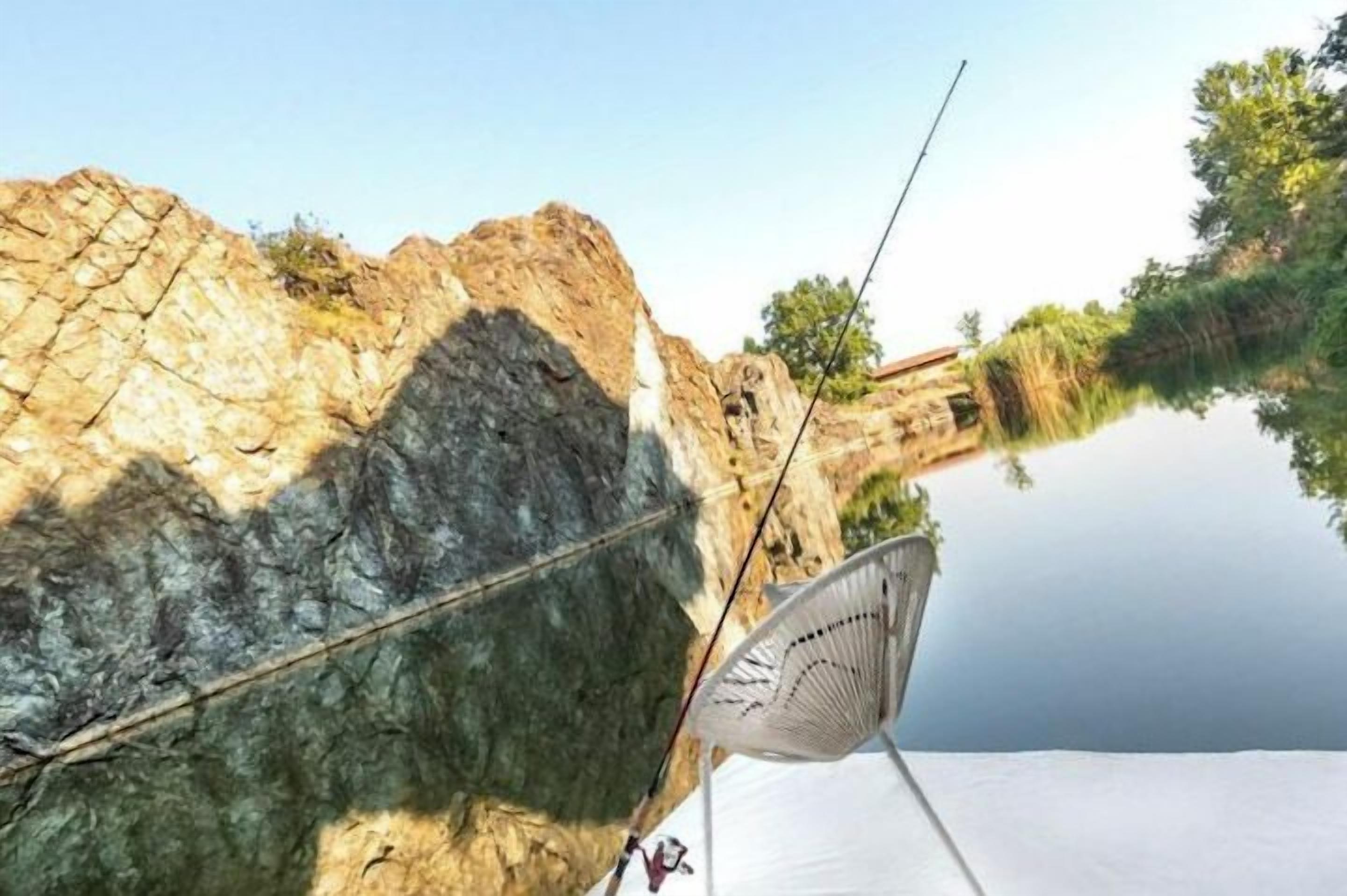 A fishing rod and fan on a tent by a calm river with rocky cliffs.