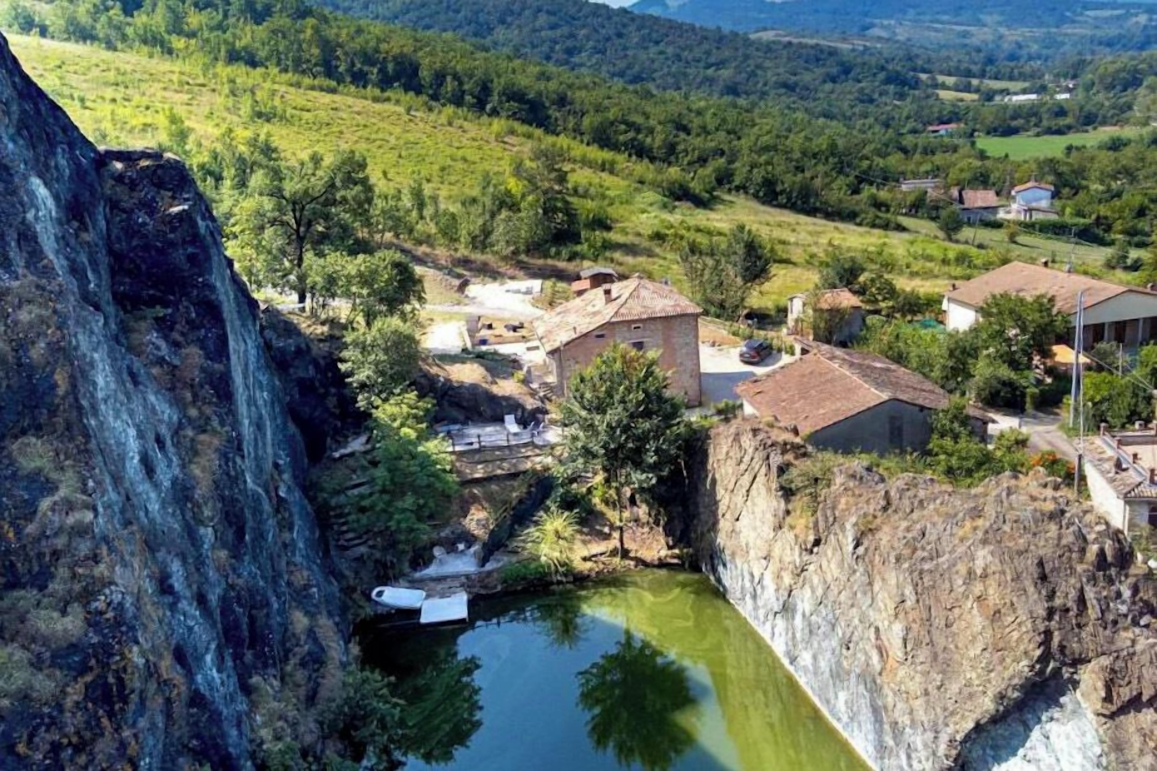 A rural village with traditional stone buildings, a small pond, and a steep cliff.