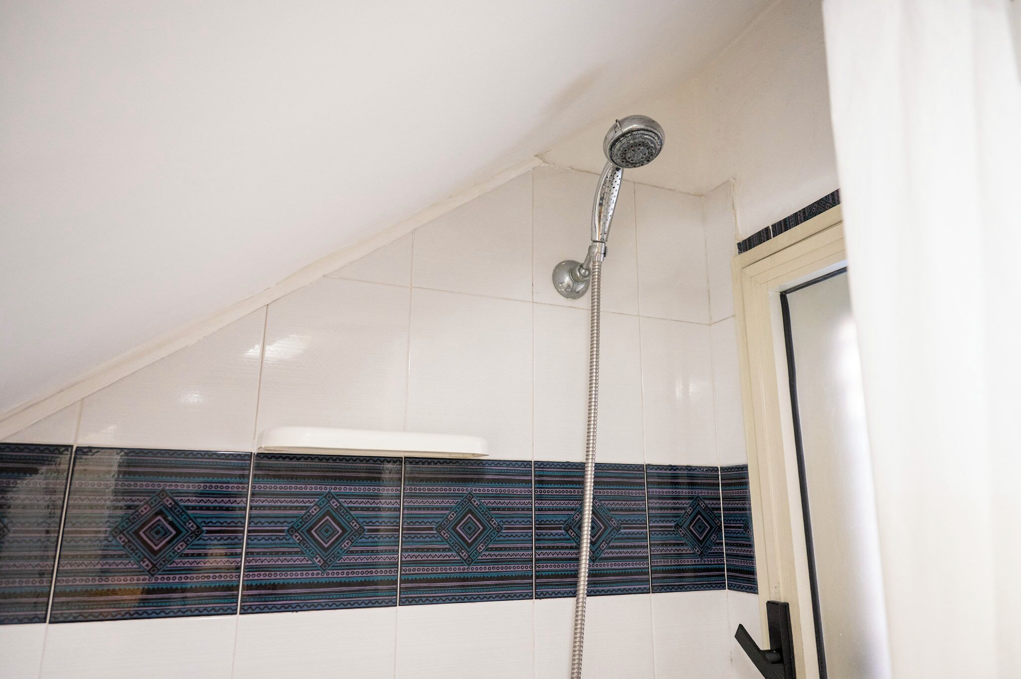 A shower with a handheld hose, white tiled walls, and decorative blue and black tiles.