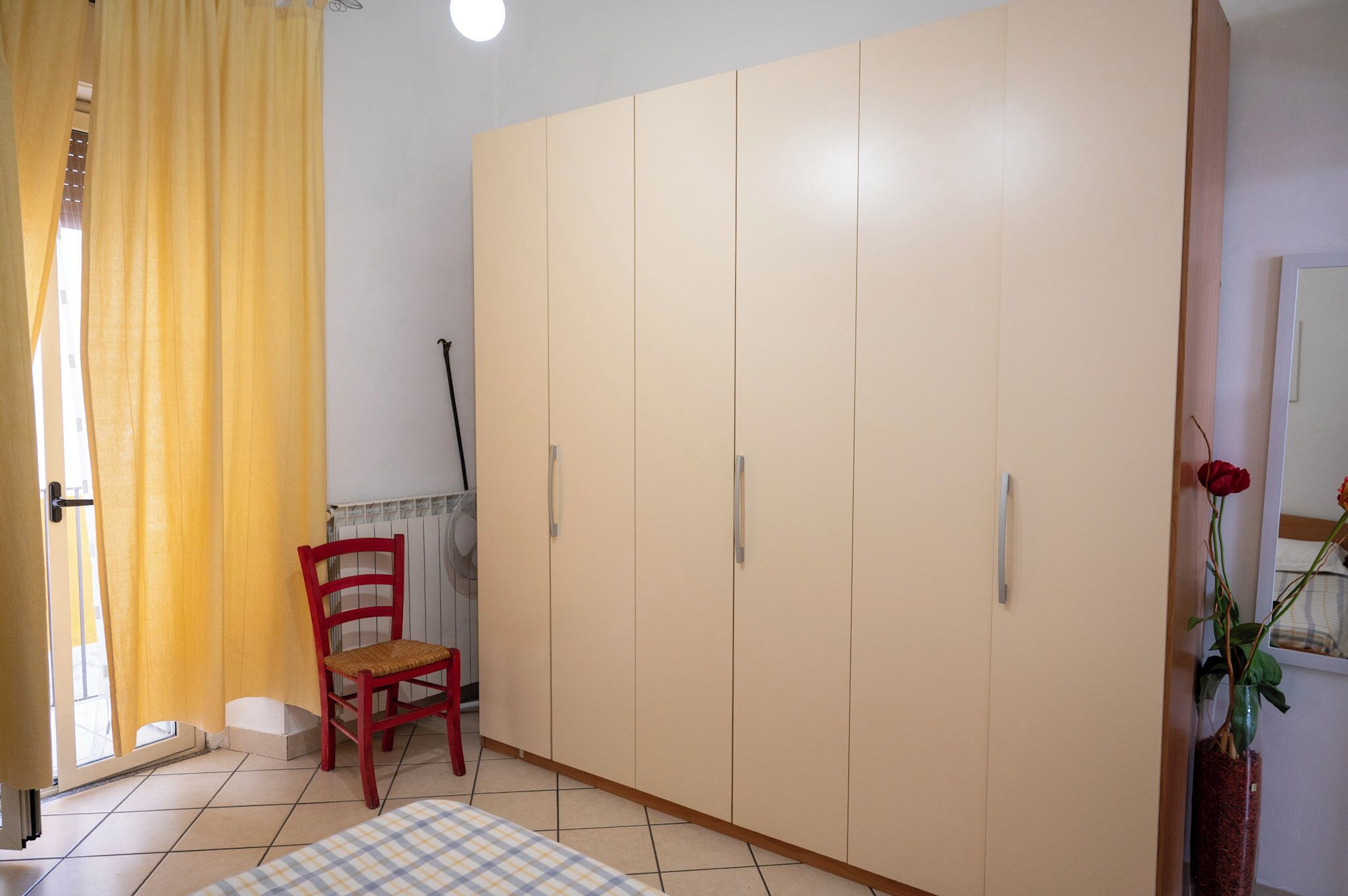 A room with a large wardrobe, a chair, a table, and a potted plant.