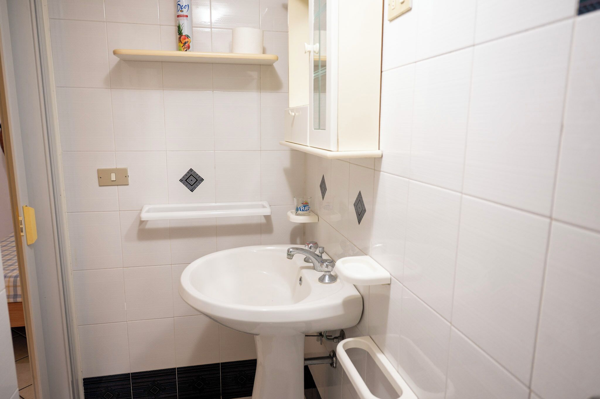 Un baño con lavamanos blanco, inodoro y repisa con artículos de aseo.