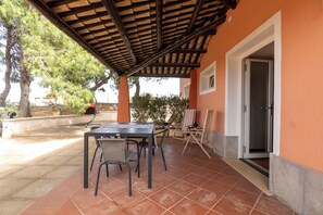 An outdoor patio with a table and chairs, a wooden pergola, and a door leading to a room. - Villa Villacolle (Marsala)