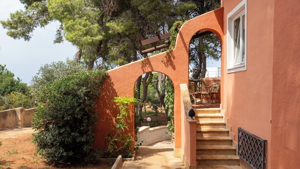 A staircase leading to a covered outdoor area with a table and chairs, surrounded by greenery and trees. - Villa Villacolle (Marsala)