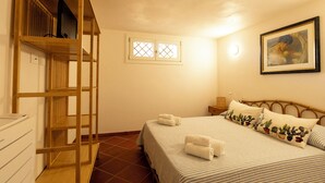 A bedroom with a bed, pillows, a wooden shelf unit, a window, and a painting on the wall. - Villa Villacolle (Marsala)