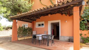 A covered patio with a table and chairs, a tiled floor, and a building with orange walls and a wooden pergola. - Villa Villacolle (Marsala)