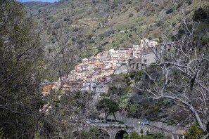 A hillside town with buildings closely packed together, a bridge, and trees in the foreground. - Casa In Montagna Vicino Al Mare (Itala)