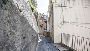 A narrow stone-paved alleyway with a stone wall on one side and a white building with a metal railing on the other. - Casa In Montagna Vicino Al Mare (Itala)