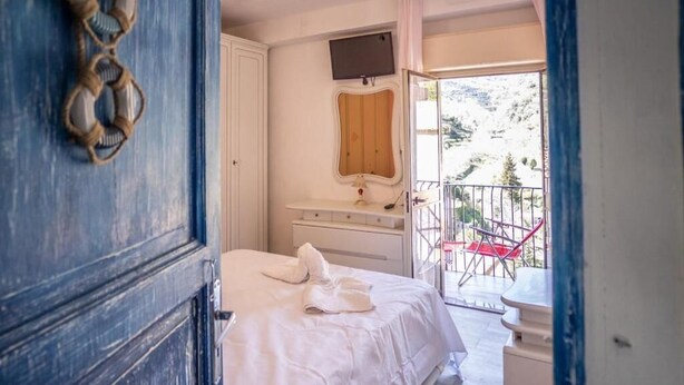 A bedroom with a bed, a dresser, a mirror, and a balcony with red chairs. - Casa In Montagna Vicino Al Mare (Itala)
