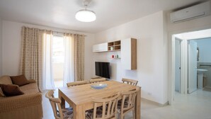 A modern living room with a wooden dining table, beige sofa, and a TV mounted on the wall. - Casa Vacanze D&G (Marina di Ragusa)