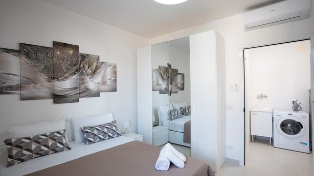 A modern hotel room with a large bed, a mirror, a washing machine, and abstract wall art. - Casa Vacanze D&G (Marina di Ragusa)