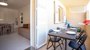 A dining area with a table set for four, a sofa, and a kitchen area with a refrigerator and a fire extinguisher. - Casa Vacanze D&G (Marina di Ragusa)